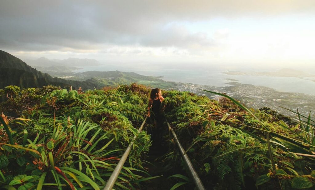 A woman hiking on a jungle trail on O‘ahu with the ocean in the background