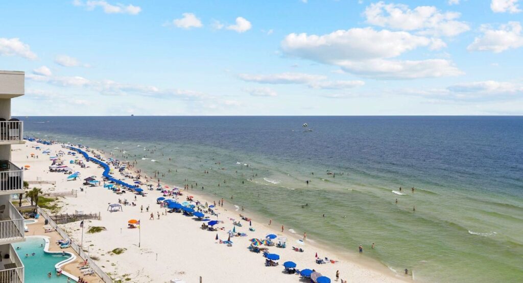 A view of the sandy beach and water on Gulf Shores with blue umbrellas dotting the sand in Gulf Shores, Alabama