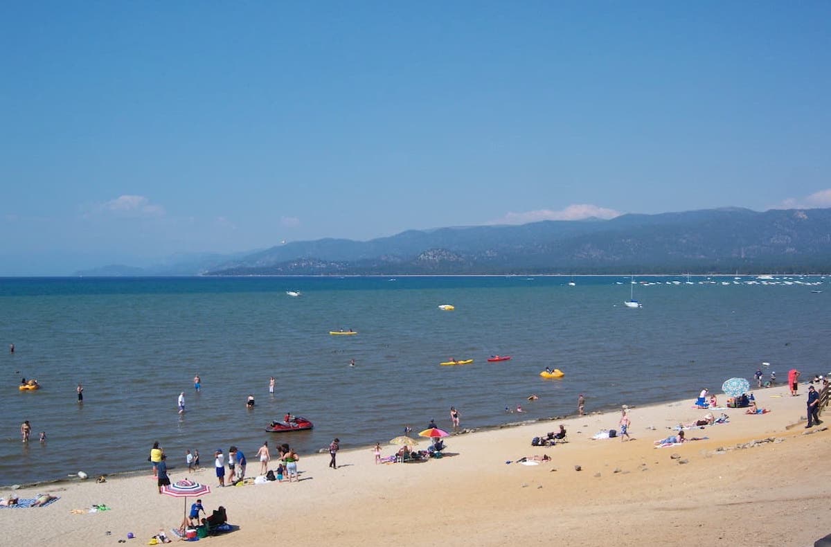 People on the El Dorado Beach and kayaks in water with mountain range in background