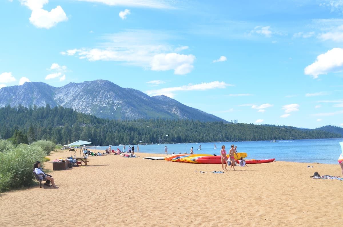 People walking on Baldwin Beach with kayaks on the sand and Mount Tallac in background