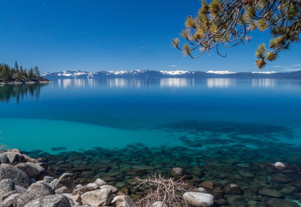 Crystal clear water of Lake Tahoe with snow capped mountains in the distance
