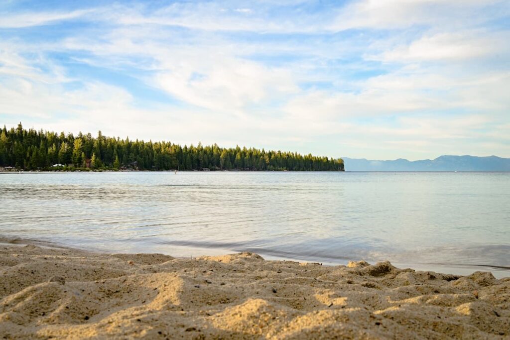 Sandy beach in Lake Tahoe with view of the water and trees and mountains in the background
