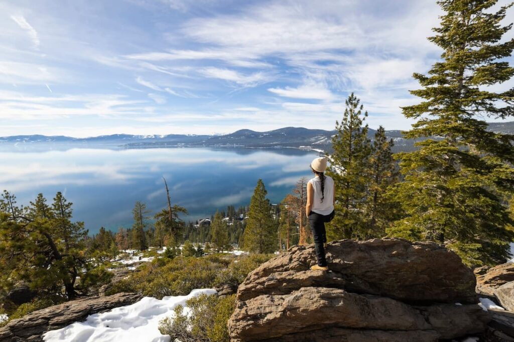Woman standing on a large rock along a hiking trail looking out onto Lake Tahoe