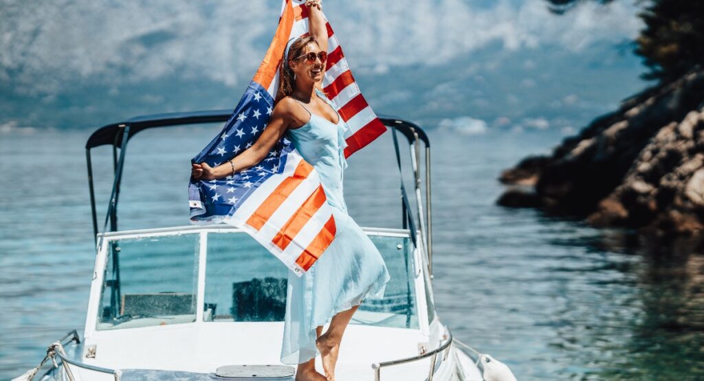 Joyful woman celebrating on a private boat, waving the US national flag with the serene backdrop of Lake Tahoe's shore.