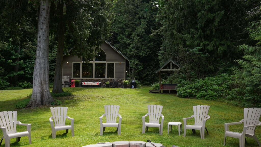 backyard of cabin with trees, grass and seating area around a fireplace