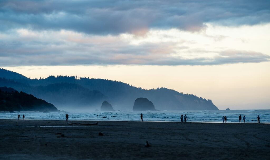 People walking along Cannon Beach with haystack rock in the background on a misty day