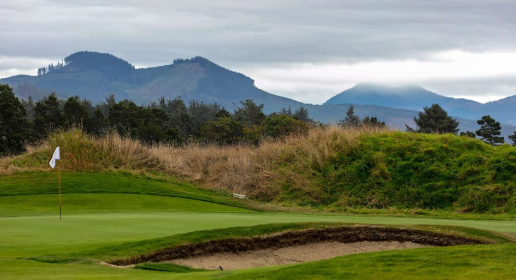 Scenic view of the lush Gearhart Golf Links with a solitary flagpole, surrounded by wild grass and overlooking the misty mountain range in Gearhart, Oregon