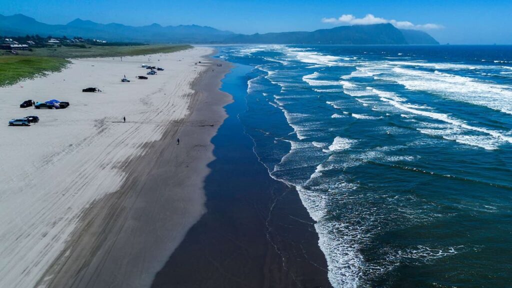 Aerial view of Gearhart Beach in Oregon, with expansive sandy coastline and vehicles parked alongside the surf