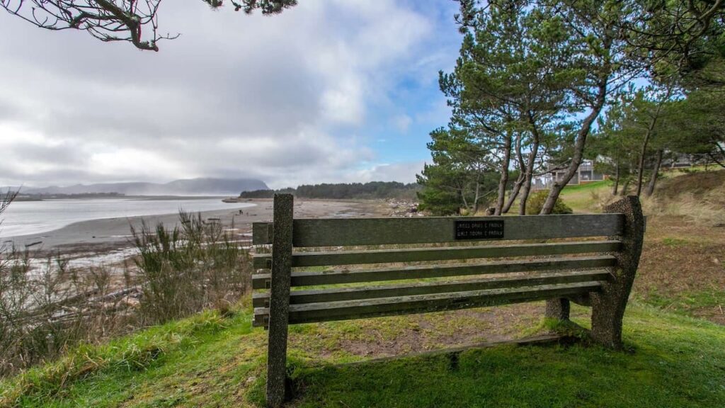 Serene view of a rustic bench overlooking the calm shores of Gearhart, Oregon. A great place for a solo traveler to meditate when seeking peace and solitude