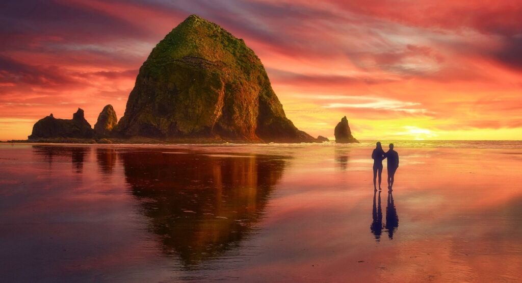 Haystack Rock at Cannon Beach during sunset with couple walking along shoreline