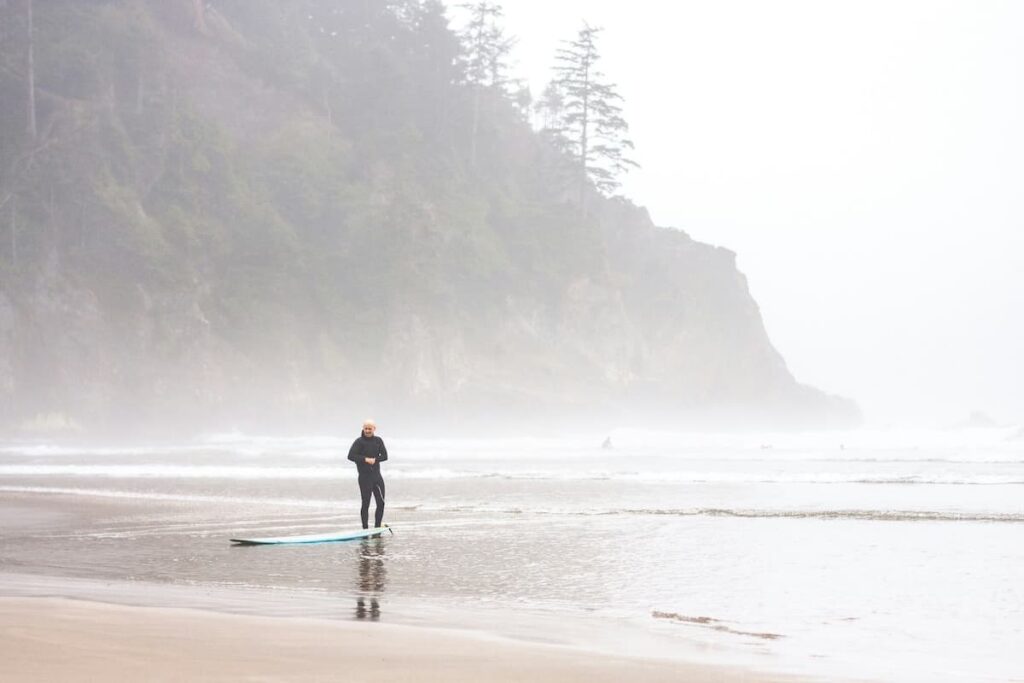 Man surfing at Short Sand beach on a foggy day with tall cliffs in the background