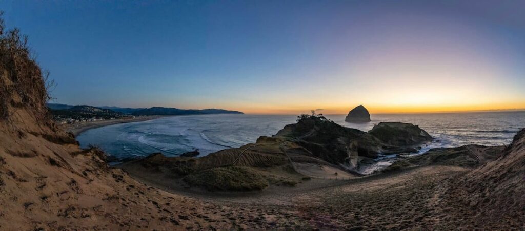 Panoramic shot of Cape Kiwanda at sunset with Haystack Rock in the water in the background