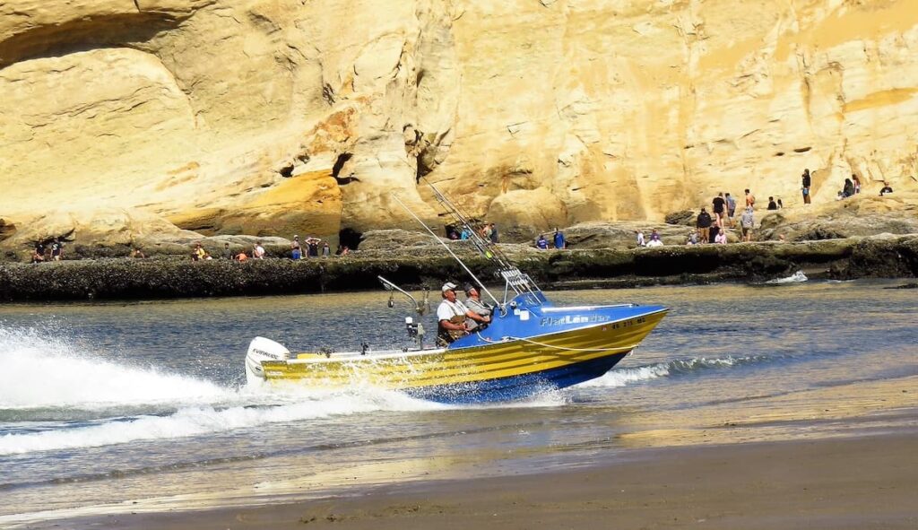 Two men driving a blue and yellow dory boat onto the shore at Pacific City