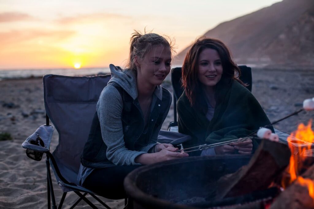 Two girls roasting marshmallows at a beach bonfire