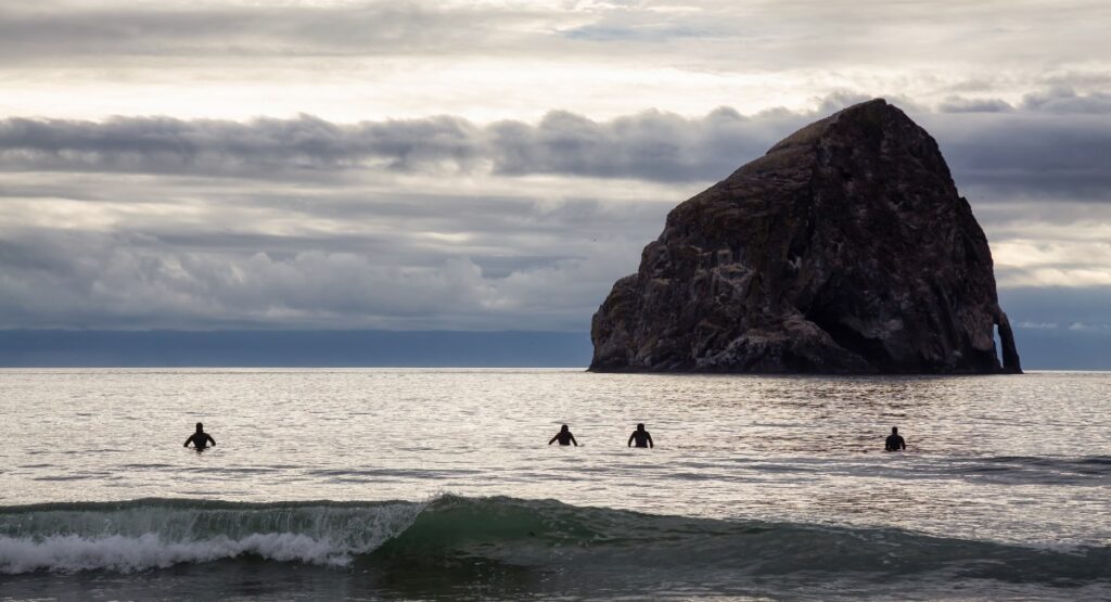 Silhouette of surfers riding gentle waves at dusk near Haystack Rock in Pacific City, ideal for a digital detox getaway