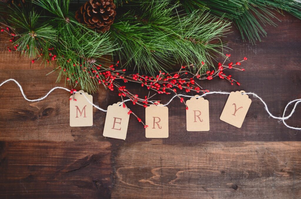 evergreen boughs with red berries on a wooden surface with the word MERRY written on a string of pennants