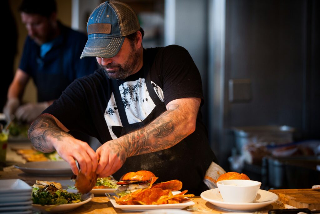 chef with tatoos and baseball hat making burgers