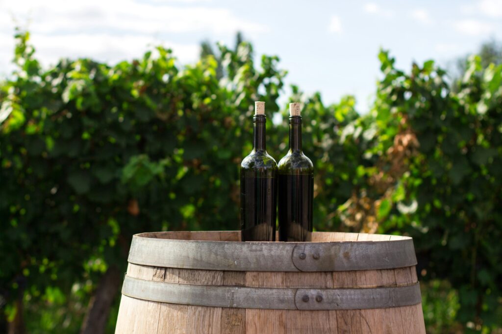 two bottles of wine on top of a barrel in front of grapevines at a vineyard