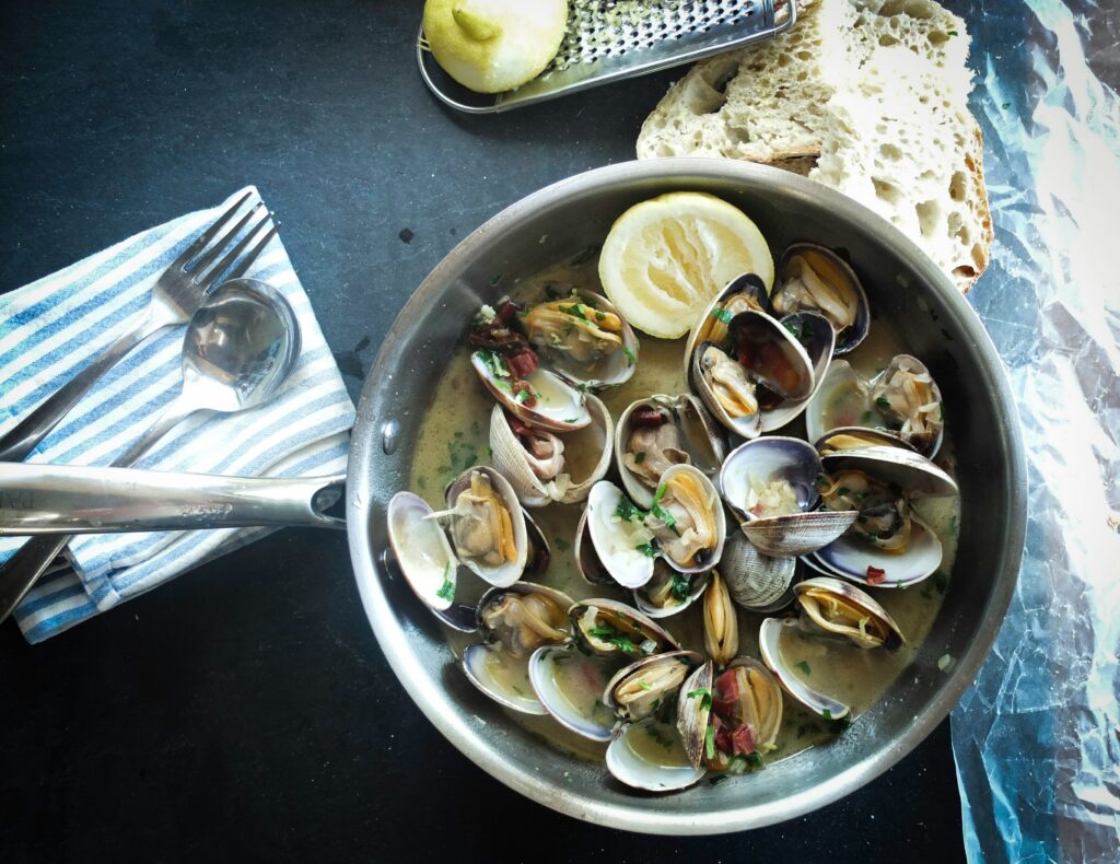 bowl of clams in broth with utensils, bread and lemon on the side - seafood Victoria BC