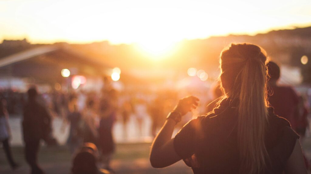 girl standing in the sunset in summer crowd in distance