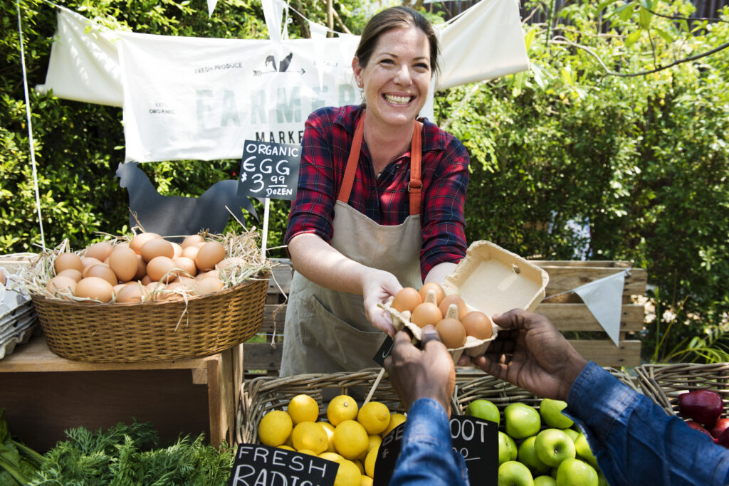 smiling woman selling produce and eggs at a farmers market